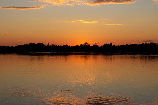 Coucher de soleil coloré et ensoleillé sur un lac calme. Le soleil se reflète à la surface de l'eau.