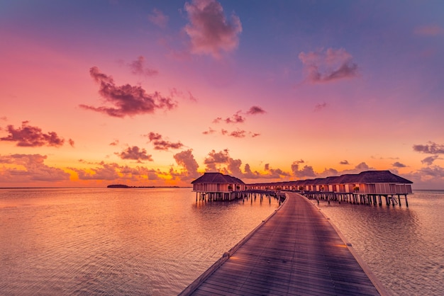 Coucher de soleil sur l'île des Maldives, complexe de villas de luxe sur l'eau et sentier de la jetée en bois. Beau ciel nuages