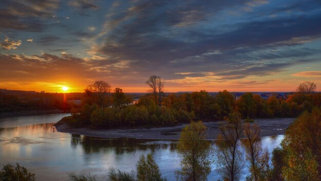 un coucher de soleil sur un lac avec des arbres et un bâtiment en arrière-plan