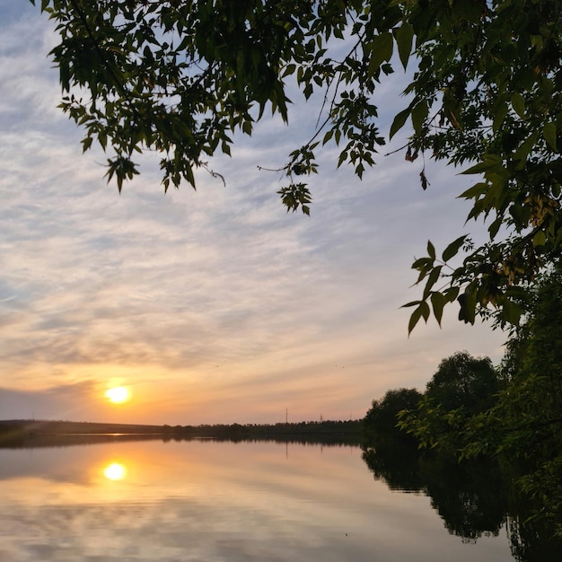 Un coucher de soleil sur un lac avec des arbres et un ciel avec des nuages