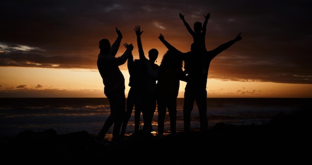 Photo coucher de soleil sur la liberté et silhouette de personnes à la plage pendant une aventure de vacances d'été ou un week-end insouciant heureux et ombre d'un groupe d'amis s'amusant ensemble au bord de l'océan en vacances