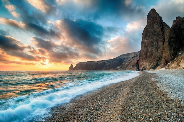 Coucher de soleil lumineux sur la mer les vagues s'écrasent sur la roche éclairée par le coucher de soleil chaud sable et cailloux volcaniques