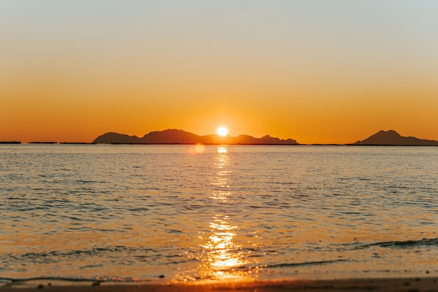 Un coucher de soleil massif sur les îles se reflétant sur l'océan avec le soleil et les marées sur la plage sur le sable au printemps, sur des tons colorés avec copie espace