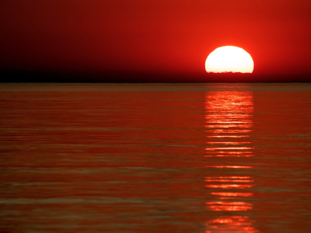 coucher de soleil en mer dans un ciel rouge avec reflet dans de petites vagues