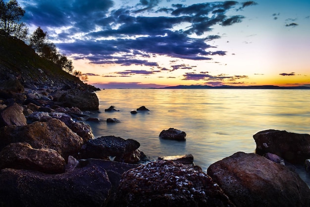 Coucher de soleil sur la mer, sur laquelle les vagues ont jeté beaucoup d'algues et de coquillages. La lumière du soleil se reflète dans