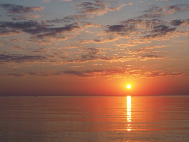 Coucher de soleil en mer avec soleil orange et reflet dans les petites vagues et les nuages illuminés