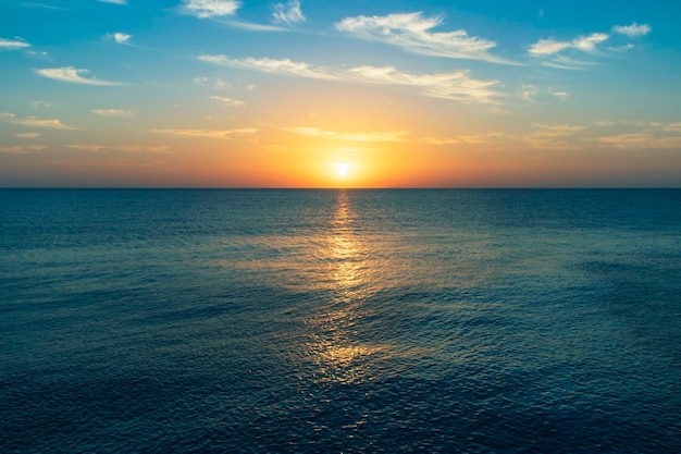 Un coucher de soleil sur l'océan avec un ciel bleu et quelques nuages