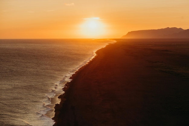 un coucher de soleil sur l'océan avec une plage et une falaise en arrière-plan