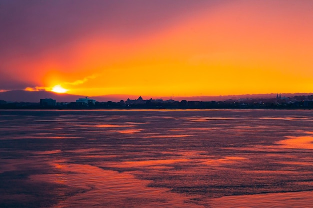 Coucher de soleil orange vif coloré dans la baie de la mer au crépuscule et la ville au loin