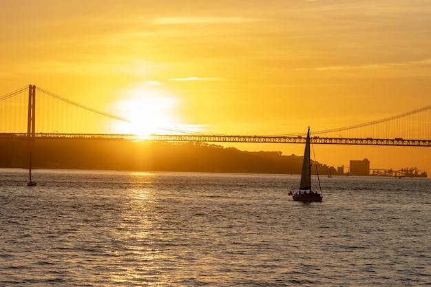 Coucher de soleil orange vif sur la rivière et un voilier flottant vers le pont