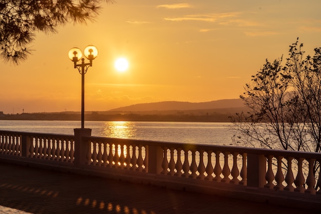 Coucher de soleil sur le quai du complexe avec balustrade et lanternes. Le soleil se couche dans les montagnes