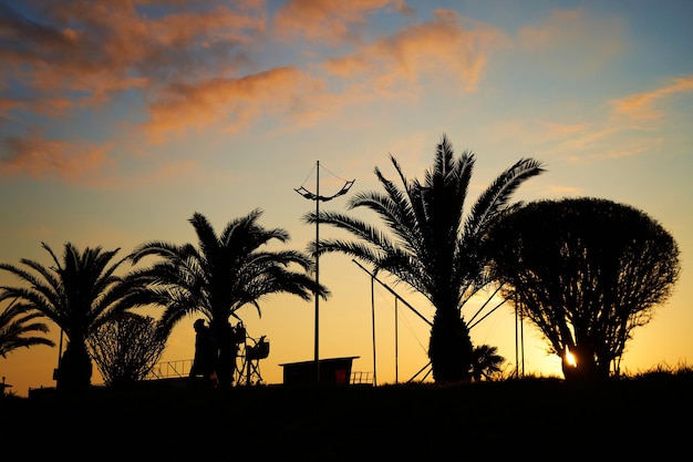 Coucher de soleil en soirée sur le remblai de la station balnéaire. Une rangée de silhouettes de palmiers sur fond de ciel brûlant