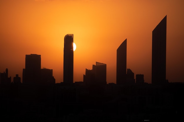 Un coucher de soleil sur une ville avec un grand bâtiment et un rayon de soleil dans le ciel