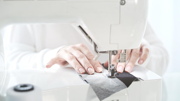 Coudre un tissu gris sur une machine à coudre blanche mains féminines