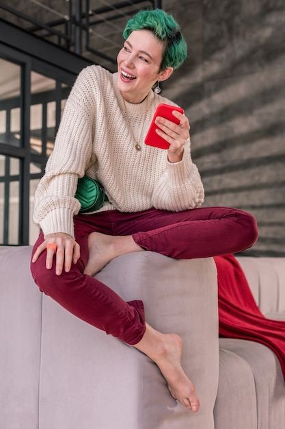 Couleur de cheveux brillante. Femme aux cheveux courts et aux cheveux de couleur vive tenant un smartphone rouge tout en écrivant un message