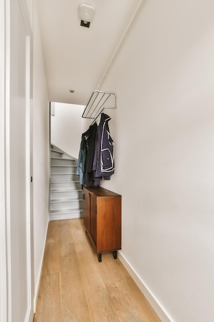 Un couloir avec parquet et murs blancs il y a un portemanteau sur le mur à côté du placard