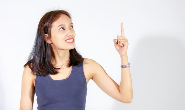 Coup de découpe en studio isolé d'une jeune mannequin asiatique en chemise à manches courtes et jeans debout tenant la main pointant le doigt sur un espace vide montrant la présentation d'une publicité de produit sur fond blanc.
