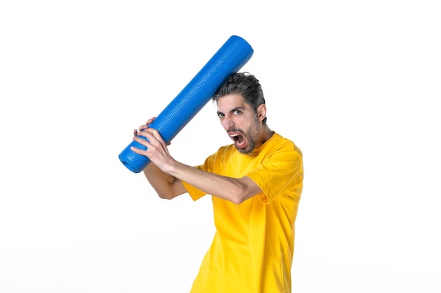 Coup de demi-corps d'un jeune homme nerveux en chemise jaune et tenant un tapis bleu plié sur la tête sur fond blanc