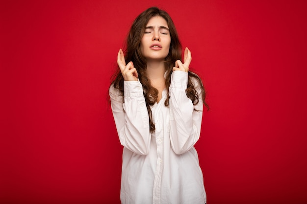 Coup de jolie jeune femme brune bouclée vêtue d'une chemise blanche isolée sur fond rouge avec