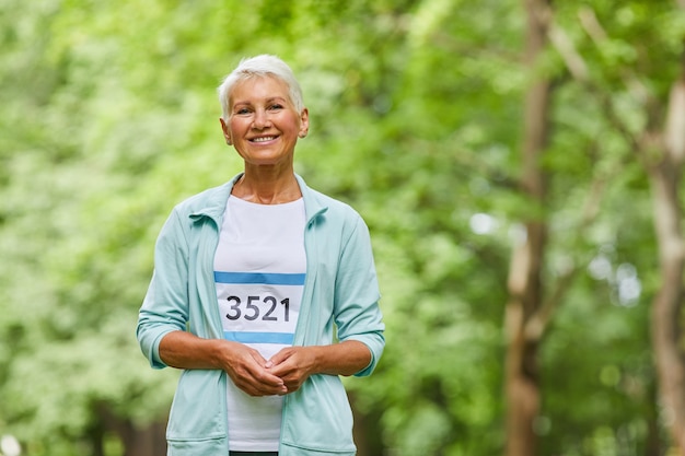 Coup de portrait moyen de femme âgée sportive gaie avec coupe courte participant au marathon d'été en regardant la caméra, copiez l'espace