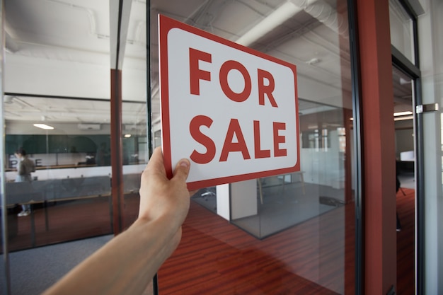 Coup de POV d'un homme méconnaissable suspendu rouge à vendre signe sur la porte en verre de l'immeuble de bureaux, copiez l'espace
