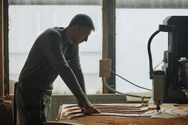 Coup de silhouette d'un charpentier masculin coupant du bois par la fenêtre dans l'espace de copie de l'atelier