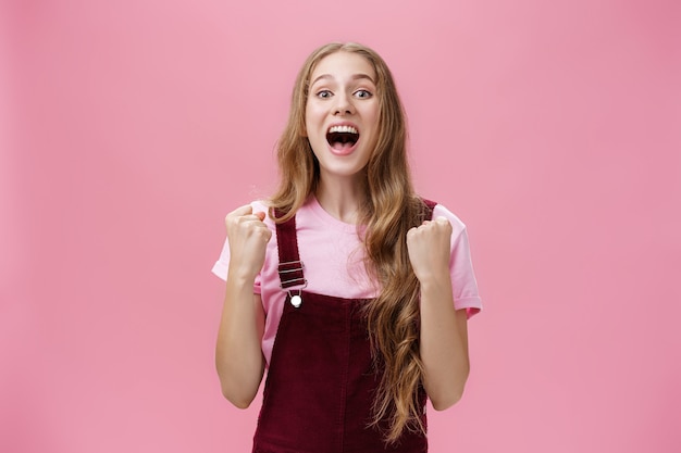 Coup de taille d'une jeune petite amie charmante et joyeuse en salopette en velours côtelé à la mode criant des poings serrés optimistes et optimistes en signe de succès et un geste de soutien criant pour l'équipe préférée.