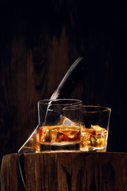 Photo une coupe d'un arbre coupé avec une hachette il y a deux verres de whisky et de la glace dessus concept de repos après une dure journée de travail whisky et bois