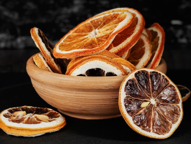 Coupe en argile avec des tranches rondes séchées d'orange et de citron sur fond sombre