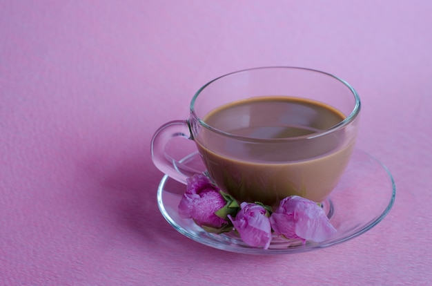 Coupe de café au lait avec trois boutons de fleur mauve sur fond rose