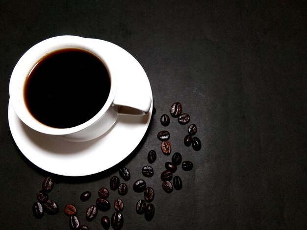 Coupe de café avec des grains de café torréfiés sur fond noir