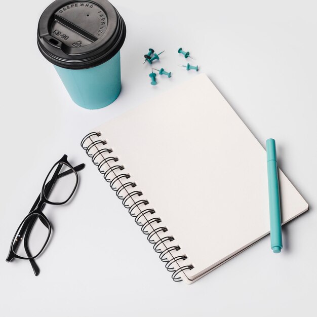 Coupe à café jetable, stylo, lunettes, bloc-notes en spirale, épingles à doigts, fond blanc