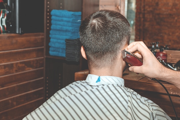 Coupe de cheveux chez le coiffeur. Barber coupe les cheveux sur la tête du client. Le processus de création de coiffures pour hommes. Un homme dans un salon de coiffure. Le plan proche. Styliste d'équipement. Mise au point sélective