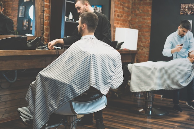 Coupe de cheveux chez le coiffeur. Barber coupe les cheveux sur la tête du client. Le processus de création de coiffures pour hommes. Un homme dans un salon de coiffure. Le plan proche. Styliste d'équipement. Mise au point sélective