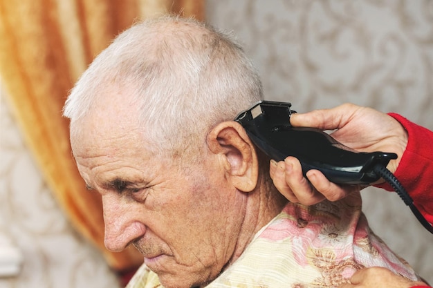 Coupe de cheveux d'un homme âgé à la maison Une femme coupe les cheveux d'un homme âgé avec une tondeuse