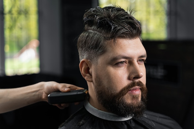 Coupe de cheveux à la machine à faible décoloration pour bel homme barbu en salon de coiffure. Coupe de cheveux avec une transition en douceur.