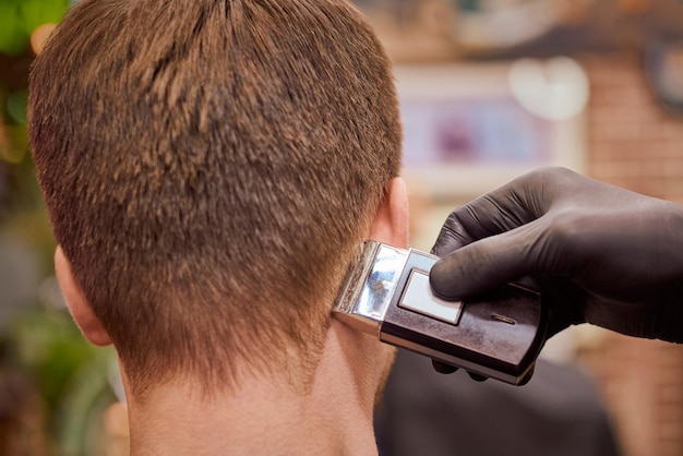 Coupe de cheveux masculine se rasant dans un salon de coiffure client se faisant couper les cheveux par un coiffeur avec un rasoir électrique