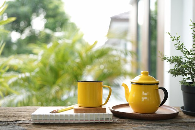 Coupe jaune et théière et sur plateau en bois et pot de plantes sur table en bois