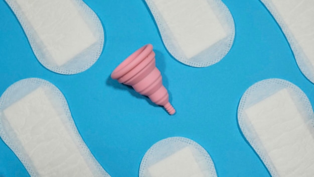 Coupe menstruelle rose pliable entre les tampons sur fond bleu. Menstruations durables