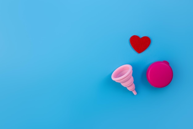 Coupe menstruelle en silicone rose flatlay Cup avec gouttes de sang et étui sur fond bleu ecofriendly