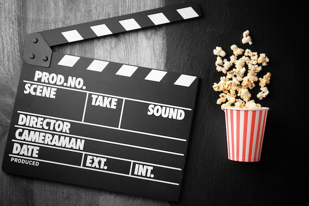 Coupe en papier avec du pop-corn et un clapper de film sur une table en bois