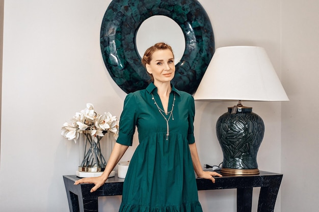 Photo coupe skinny et femme souriante sexuelle vêtue d'une robe verte et de bijoux et posant à côté d'une table dans une maison. belle coiffure