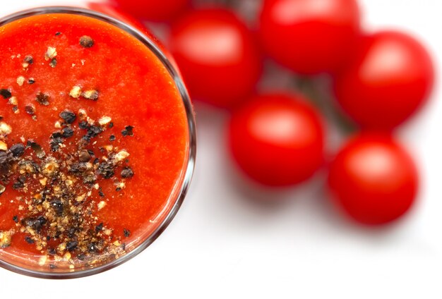 Coupe en verre avec du jus de tomate avec du poivre noir moulu et des tomates cerises sur fond blanc