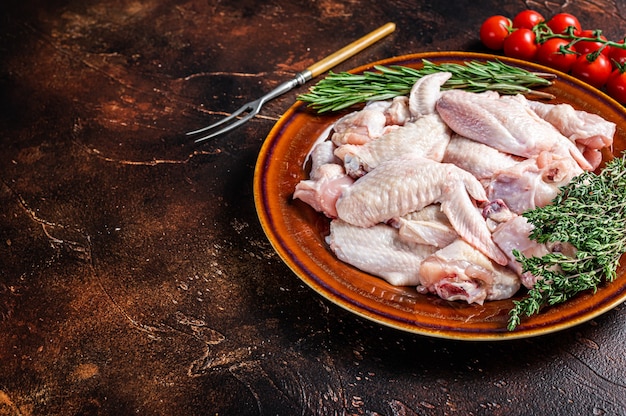 Couper les ailes de poulet cru dans une assiette rustique avec du thym et du romarin. Fond sombre. Vue de dessus. Copiez l'espace.