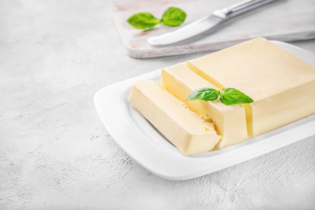 Couper le bloc de beurre frais dans un plat à beurre en céramique blanche sur blanc