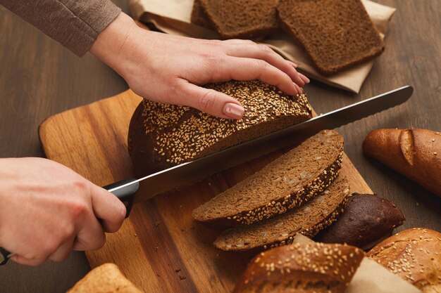 Couper du pain sur planche de bois. Chef féminin méconnaissable préparant des sandwichs sains, vue de dessus, espace de copie