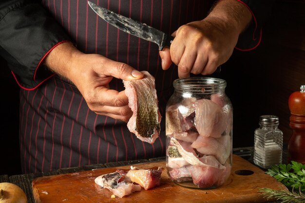 Photo couper du poisson carpe cru pour préparer du hareng dans un pot ou en conserve couteau dans la main du cuisinier et steak avec du poisson