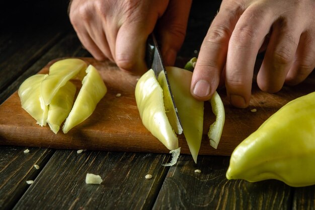 Couper du poivre pour un plat de légumes avec un couteau dans les mains d'un chef l'idée de cuisiner un régime végétal sur la table de cuisine dans un restaurant