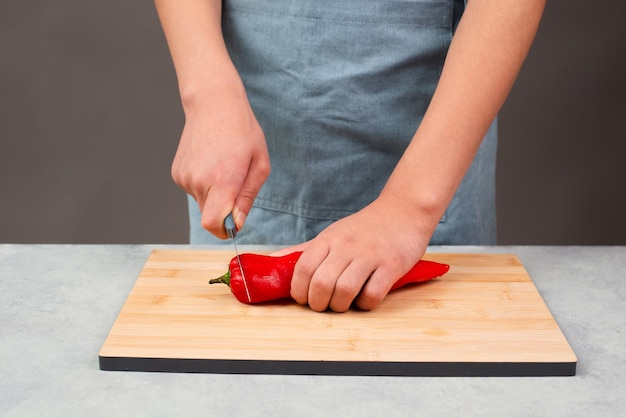 Couper du poivron rouge sur une planche de bois préparer des aliments sains avec des légumes frais au paprika