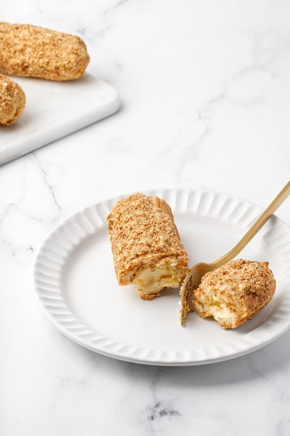 Couper l'éclair à la vanille Dessert avec de la crème avec une fourchette sur une plaque blanche sur fond de marbre